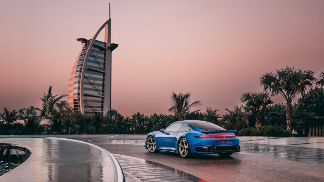 A static Porsche 911 in blue with the Burj Al Arab in the background