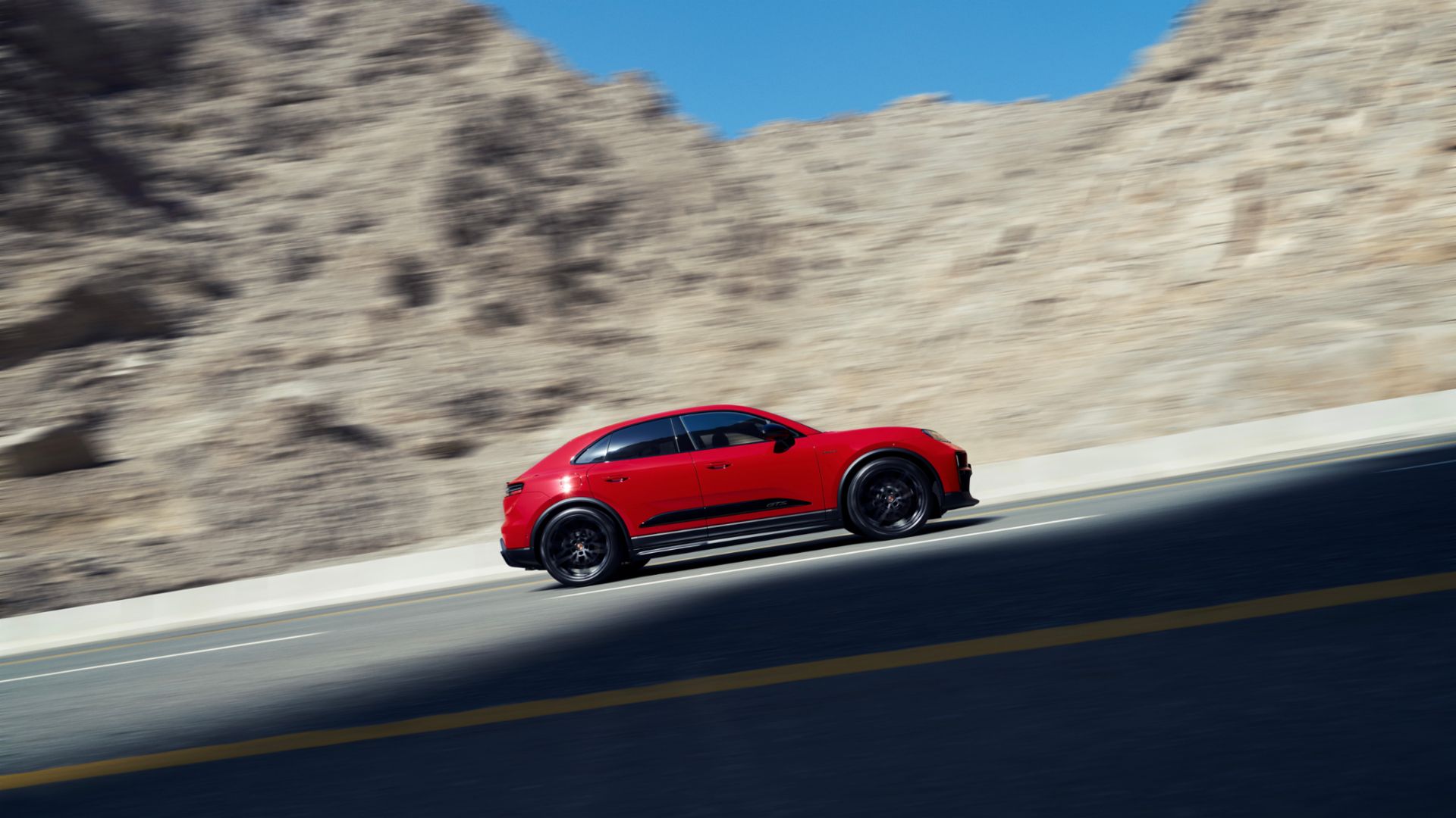 Dynamic side shot of a red Porsche Macan GTS Electric in a mountainous backdrop.