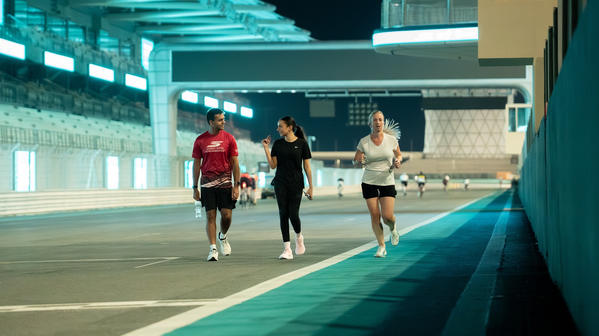Two people walk while one runs at the Yas Marina Circuit