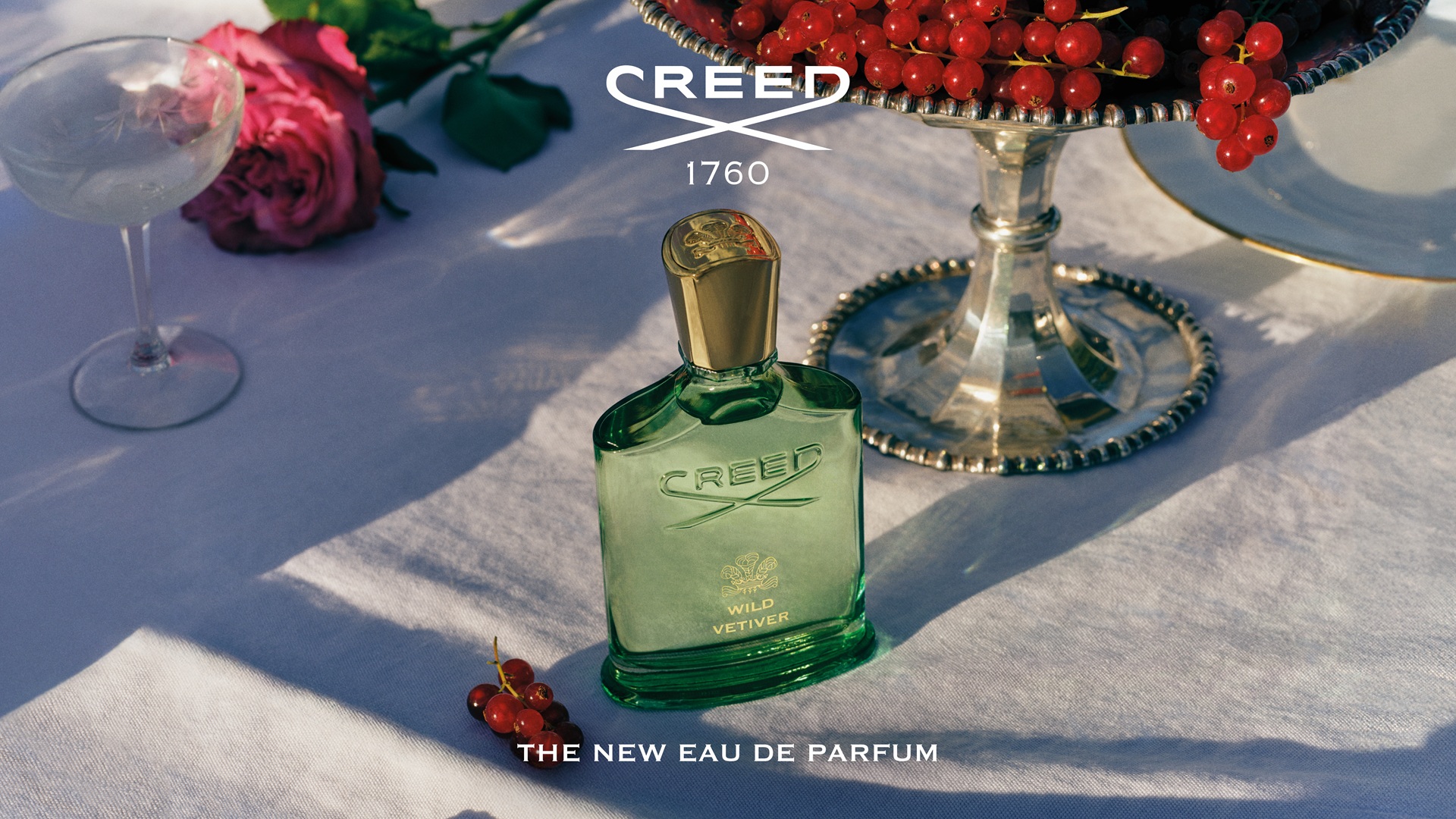 The green bottle of the Wild Vetiver by The House of Creed kept on a table alongside roses and berries