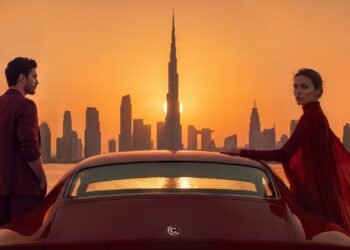 Connoisseur Collective Dubai: An image that shows the Dubai skyline with two models standing on either side of a red car.